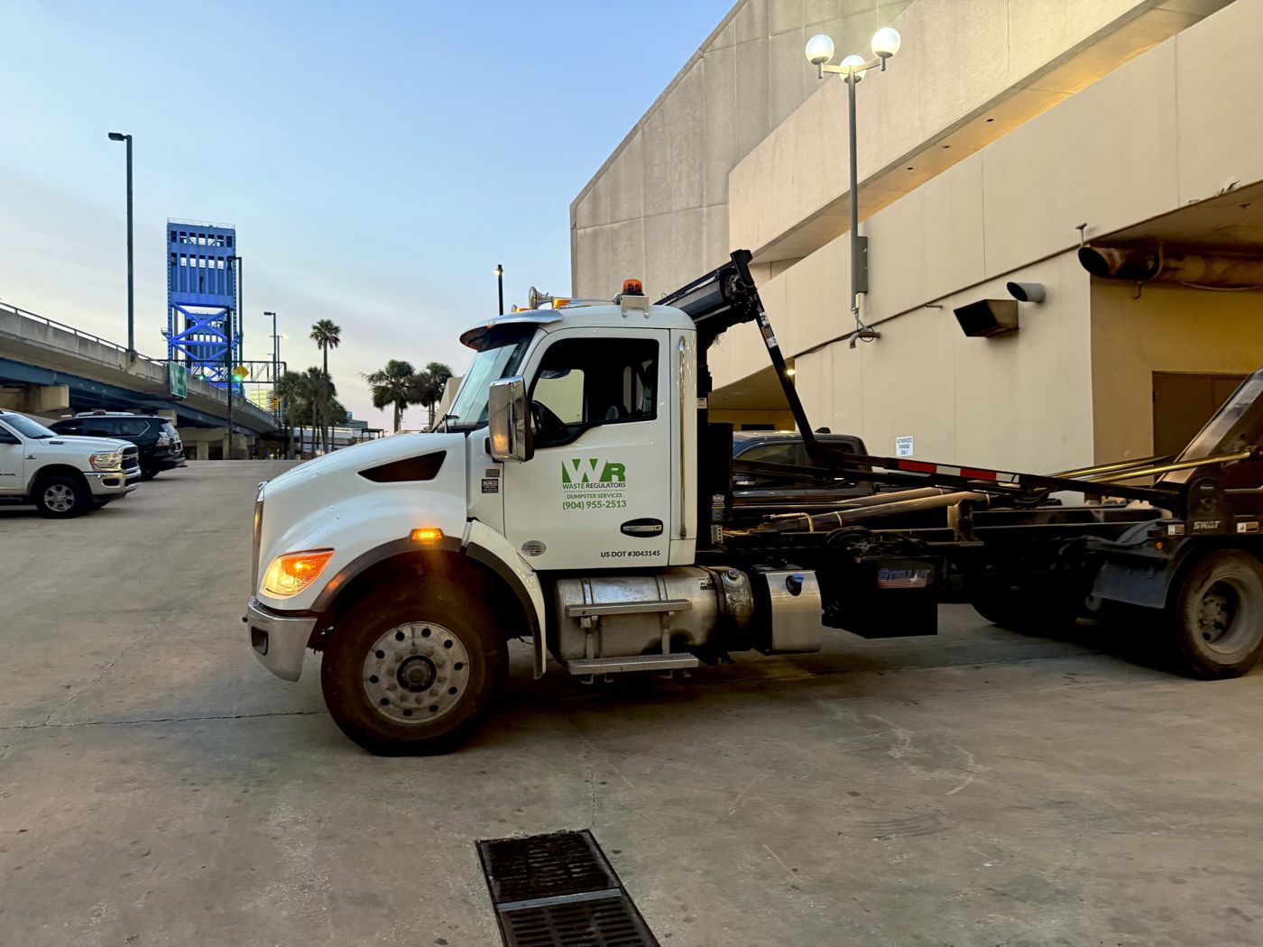 Waste Regulators roll-off truck in downtown Jacksonville with the Main Street Bridge behind it